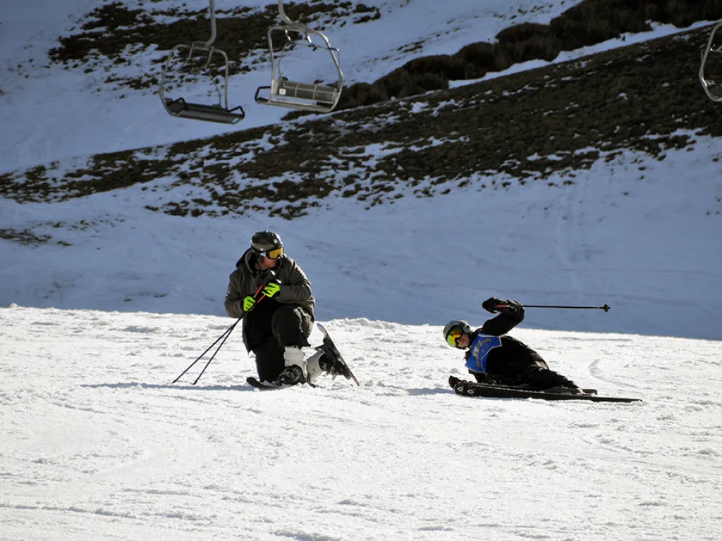 Zwei Skifahrende am Hang, eine Person kniet im Schnee.